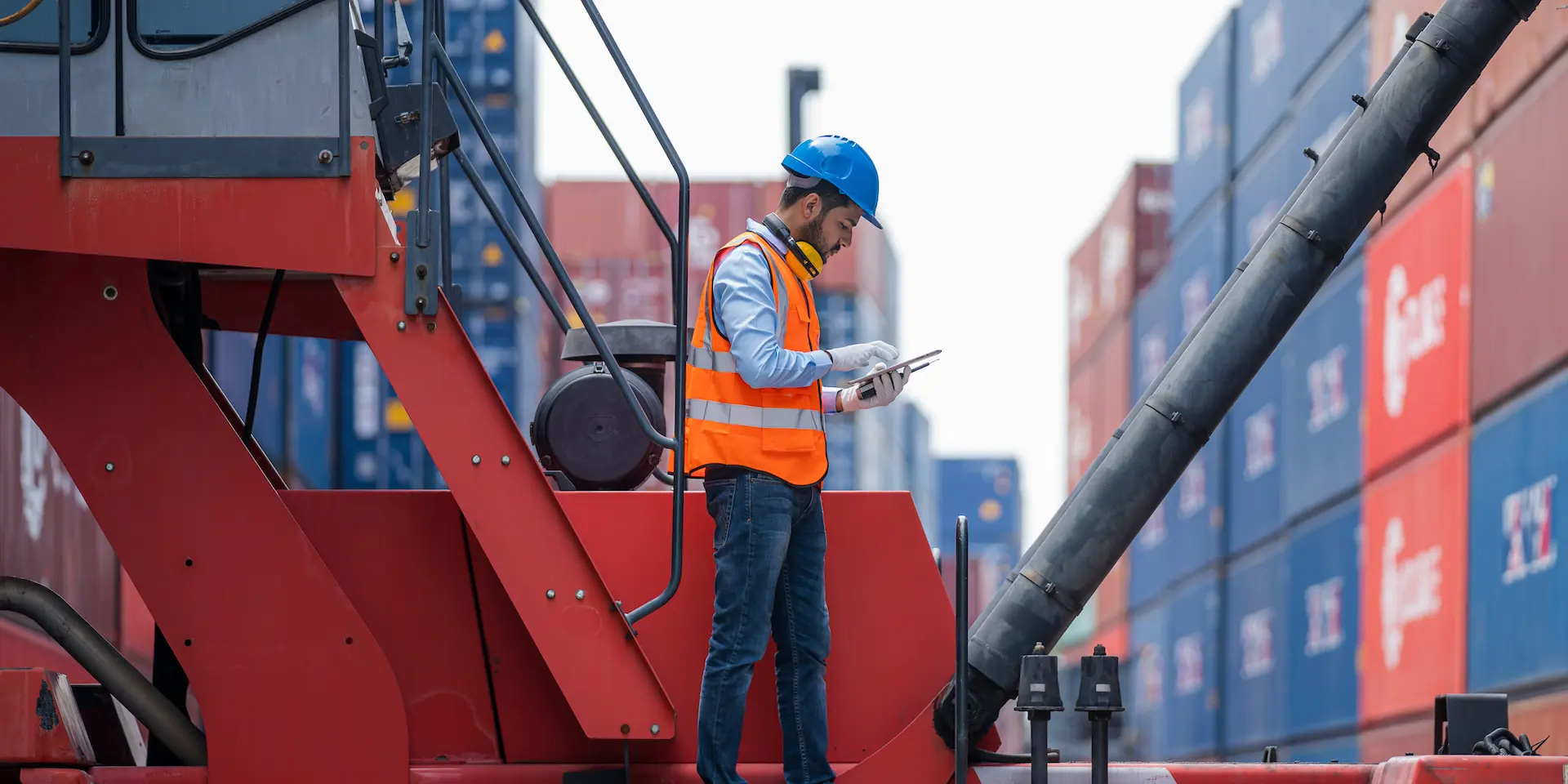 Stacked shipping containers at a terminal with an inspector in hi-vis checking a tablet
